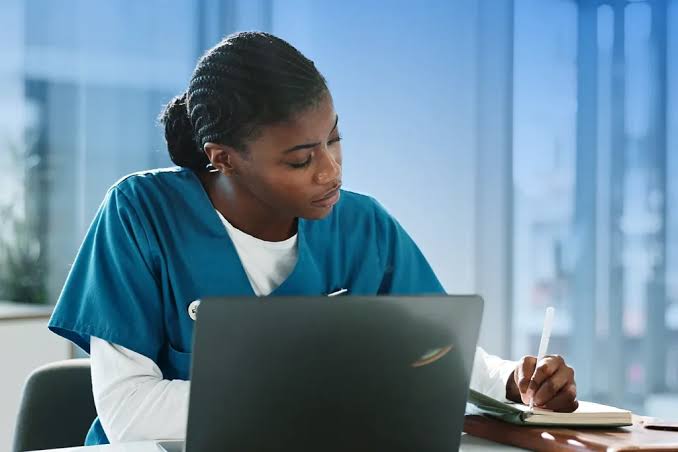 Nurse writing notes at a desk with a laptop